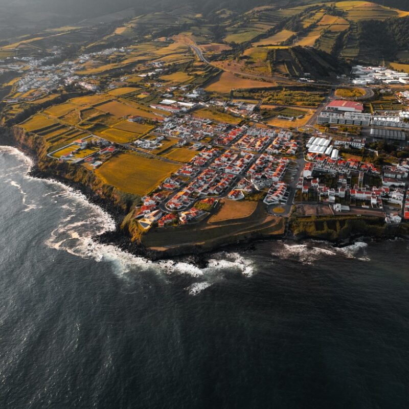 From above drone view of Villa Franca do Campo village with small houses located on shore of Atlantic ocean , with rippling water and foamy waves in summer day in Portugal