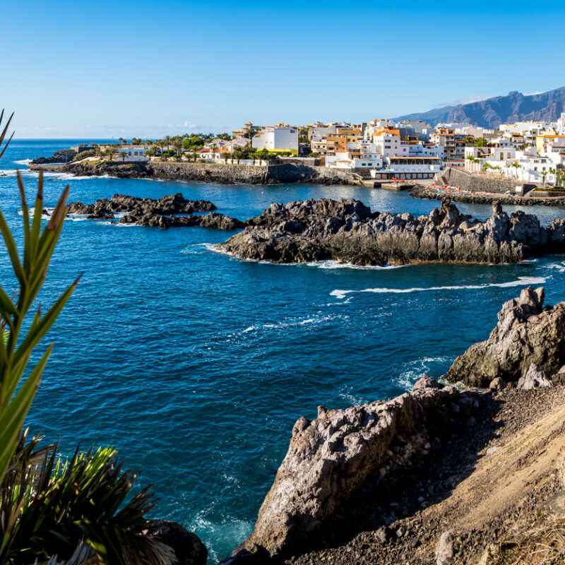 Panoramic view of the idyllic Tenerife fishing village of Alcalá, framed by a rocky coastline with Playa de Alcalá beach at the Atlantic Ocean and the Montana de Guama mountain in the background.